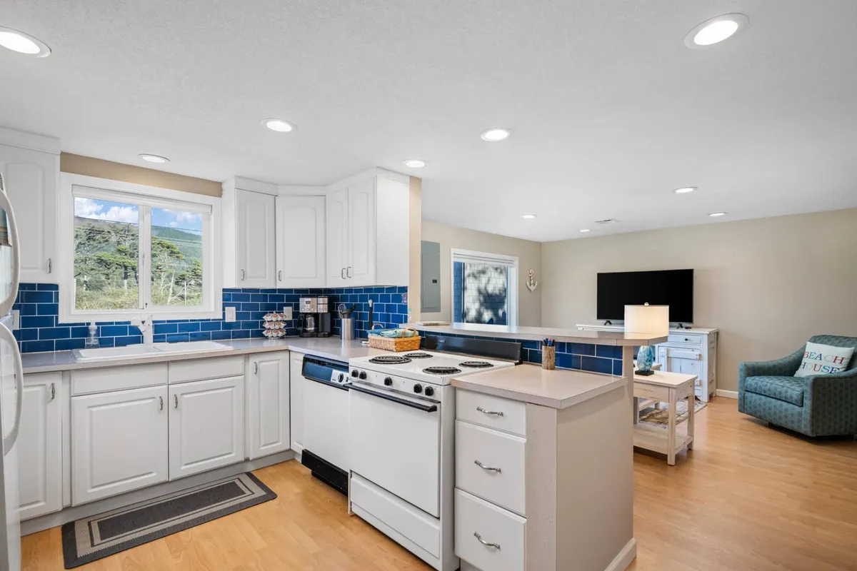A cheerful kitchen with a striking blue tile backsplash, crisp white cabinetry, a central kitchen island, and a large window that floods the space with light. The kitchen feels fresh and inviting, perfect for cooking and entertaining.