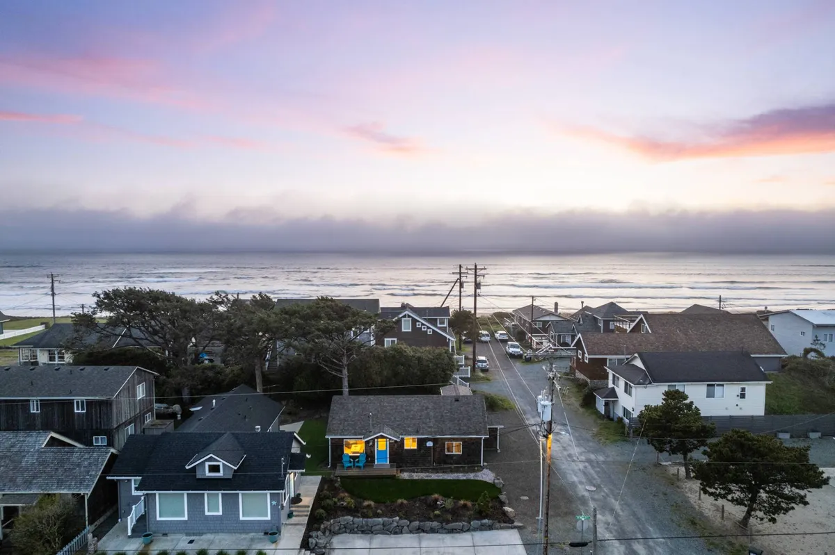 This image captures a serene coastal scene with a sunset sky, ocean views, and cozy homes nestled along the shoreline. The scene evokes the tranquility and beauty of the Oregon coast, perfect for relaxing after a day of outdoor adventures.