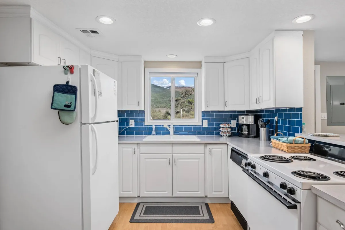 A bright, cheerful kitchen with a blue tiled backsplash, window views of the mountains, and modern appliances. The space is well-suited for preparing family meals or cooking up a fresh seafood feast with your catch of the day.