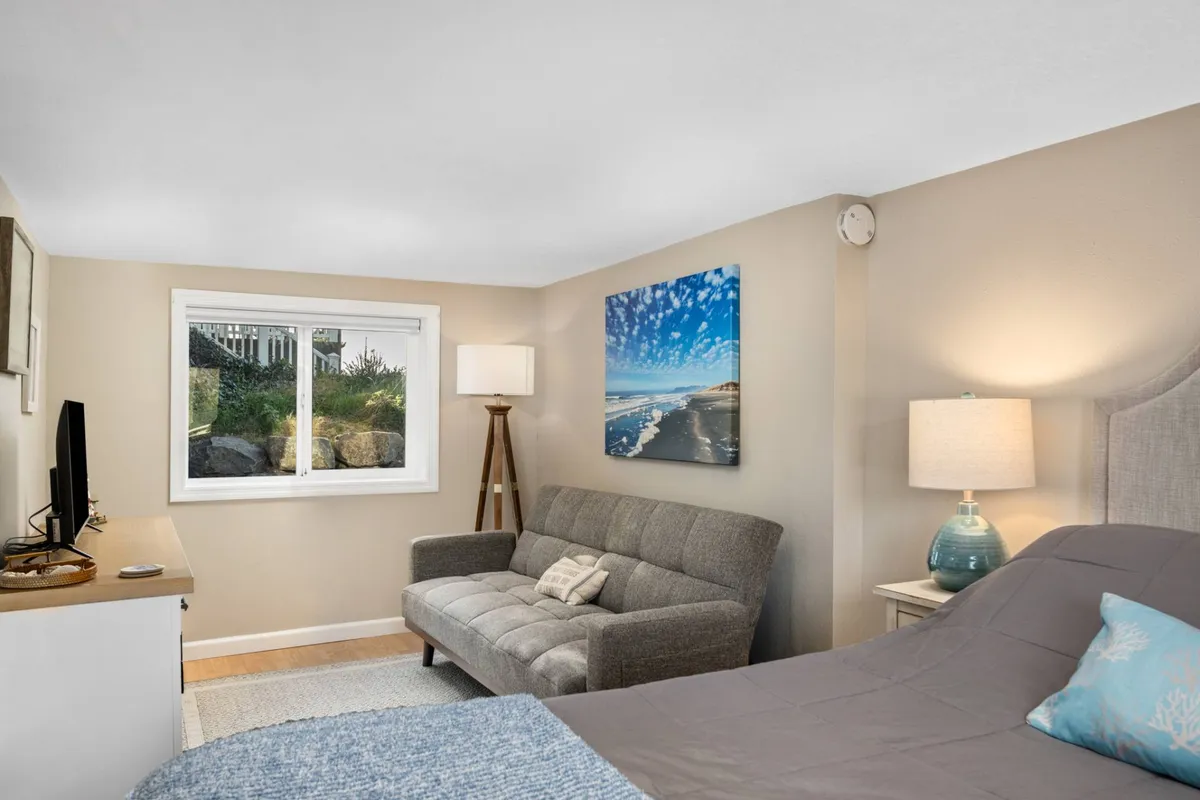 This image features a cozy bedroom with a plush queen bed positioned near a window, allowing natural light to fill the space. A comfortable sleeper couch is also visible, complemented by serene artwork and soft furnishings, creating a welcoming and restful atmosphere ideal for families.