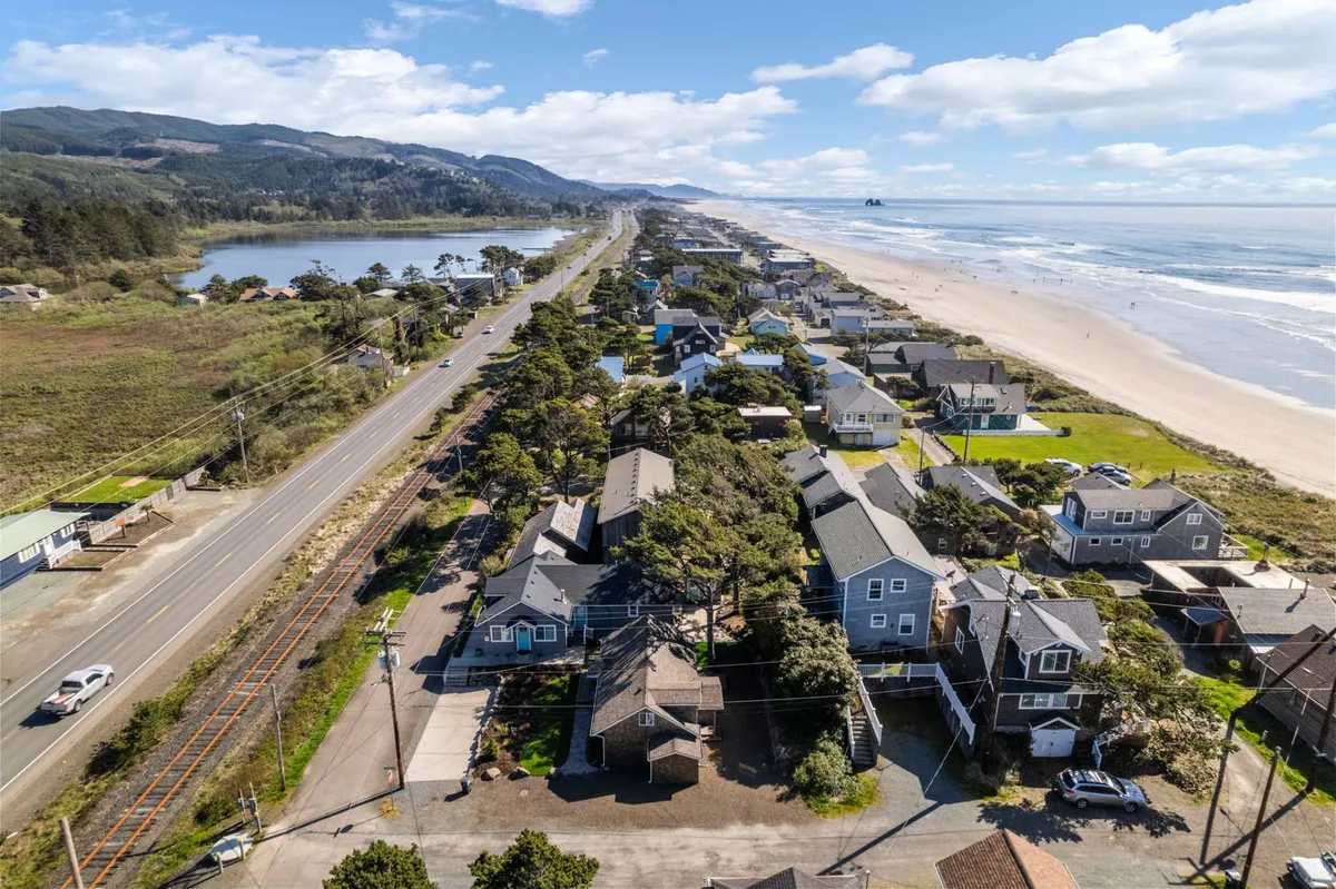 A panoramic view featuring coastal houses lining the beach, the expansive ocean, and nearby hills, with a road running along the scenic coastline. The image evokes a sense of adventure, with spaces for sandcastle building, family walks, and exploring the surroundings.